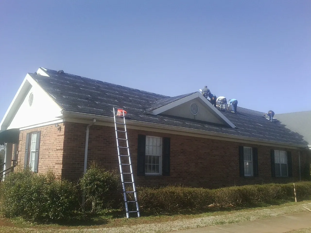 Crew tearing shingles off a brick ranch roof with a ladder set — Emergency Roof Repair work by our crew in Groveland