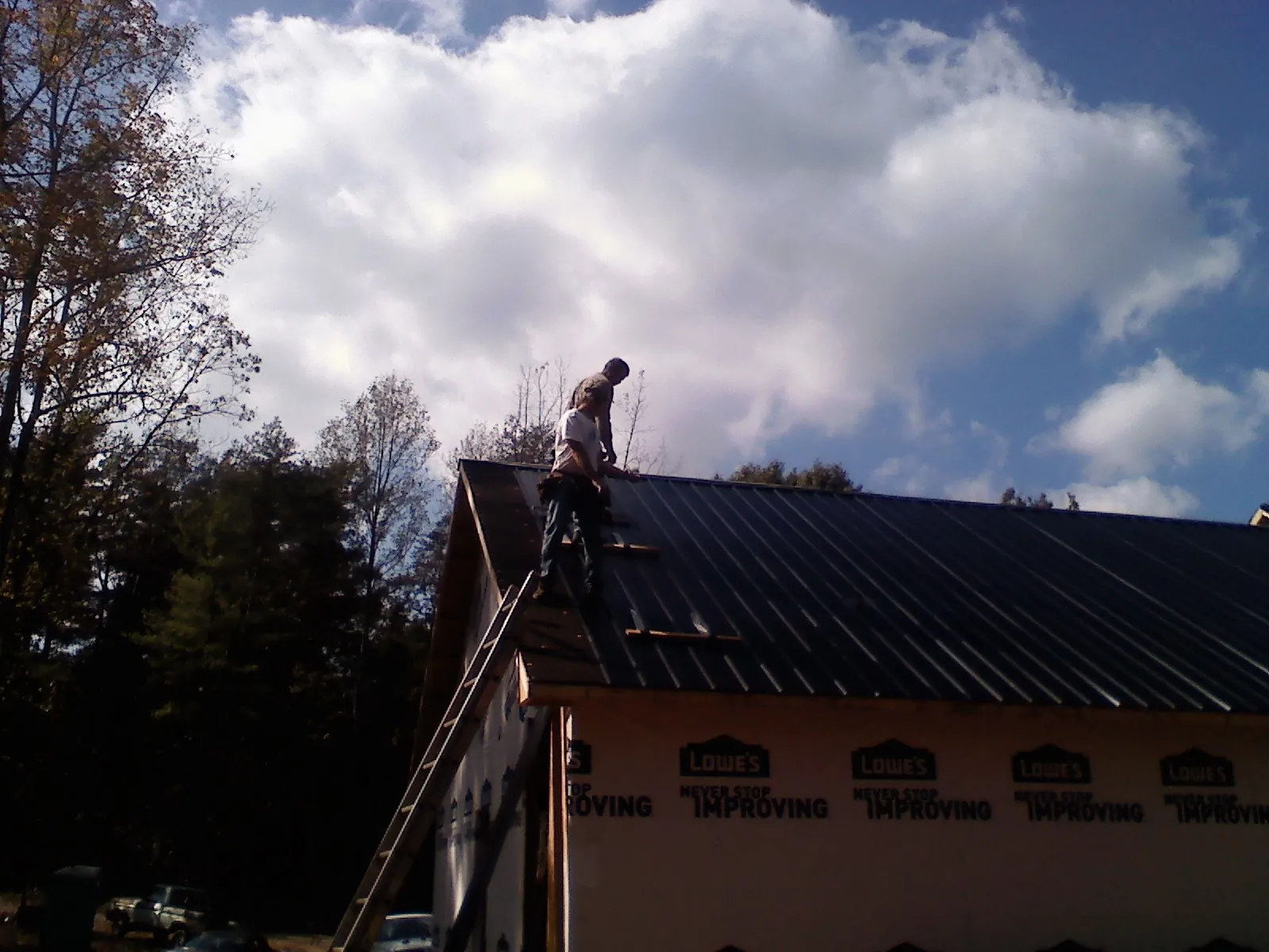 Roofer fastening dark metal panels high against a cloudy sky, from a Roof Inspection job in Groveland